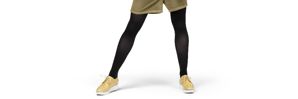 A person's legs wearing black tights, olive green shorts, and tan sneakers, shown from the waist down against a plain white background.